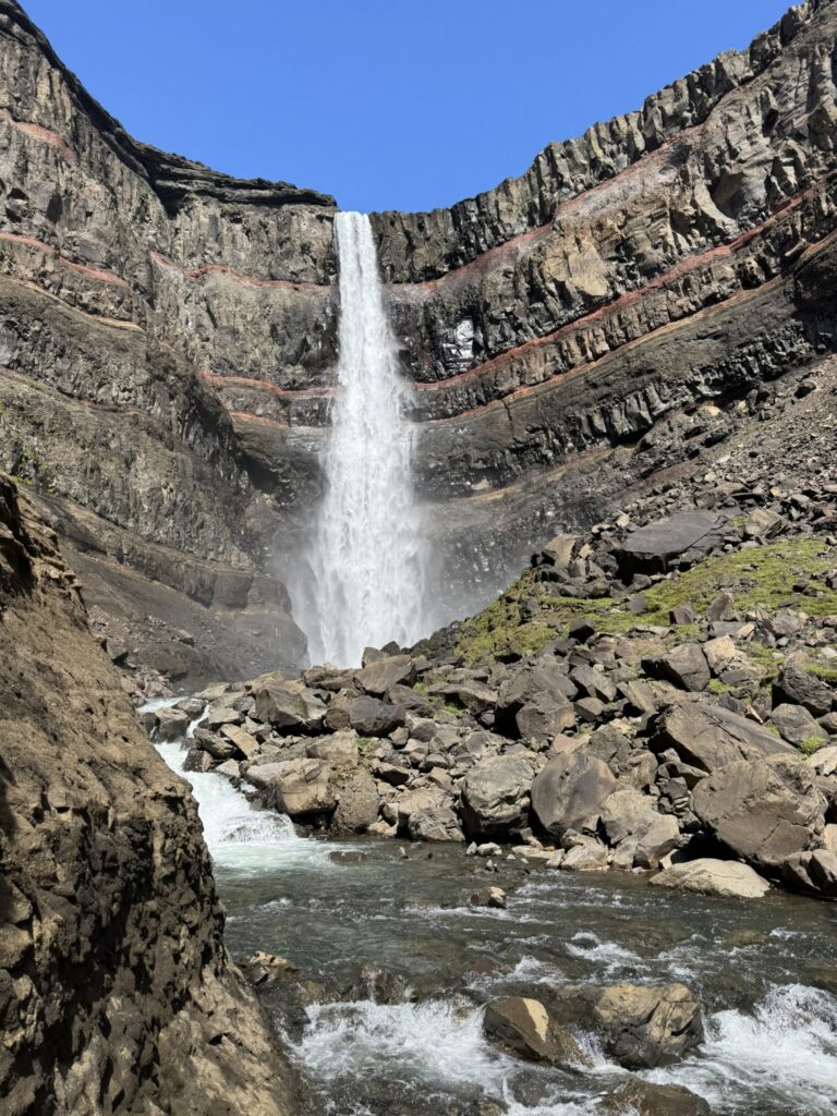 The tall Hengifoss waterfall in East Iceland featuring striking red clay layers between basaltic rock strata