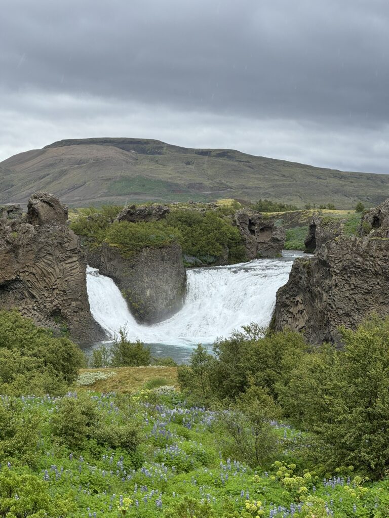 The unique twin cascades of Hjálparfoss waterfall meeting in a pool surrounded by basalt formations in South Iceland