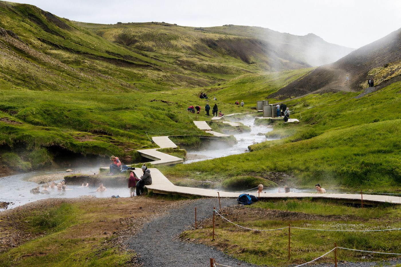 People soaking in the Reykjadalur thermal river in Iceland, with wooden boardwalks and steaming hillsides